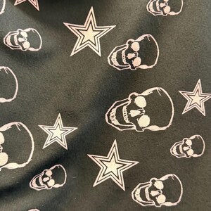 May include: Dark fabric featuring a repeating pattern of white skulls and stars. The skulls have open eye sockets and teeth. The stars have a five-point design.