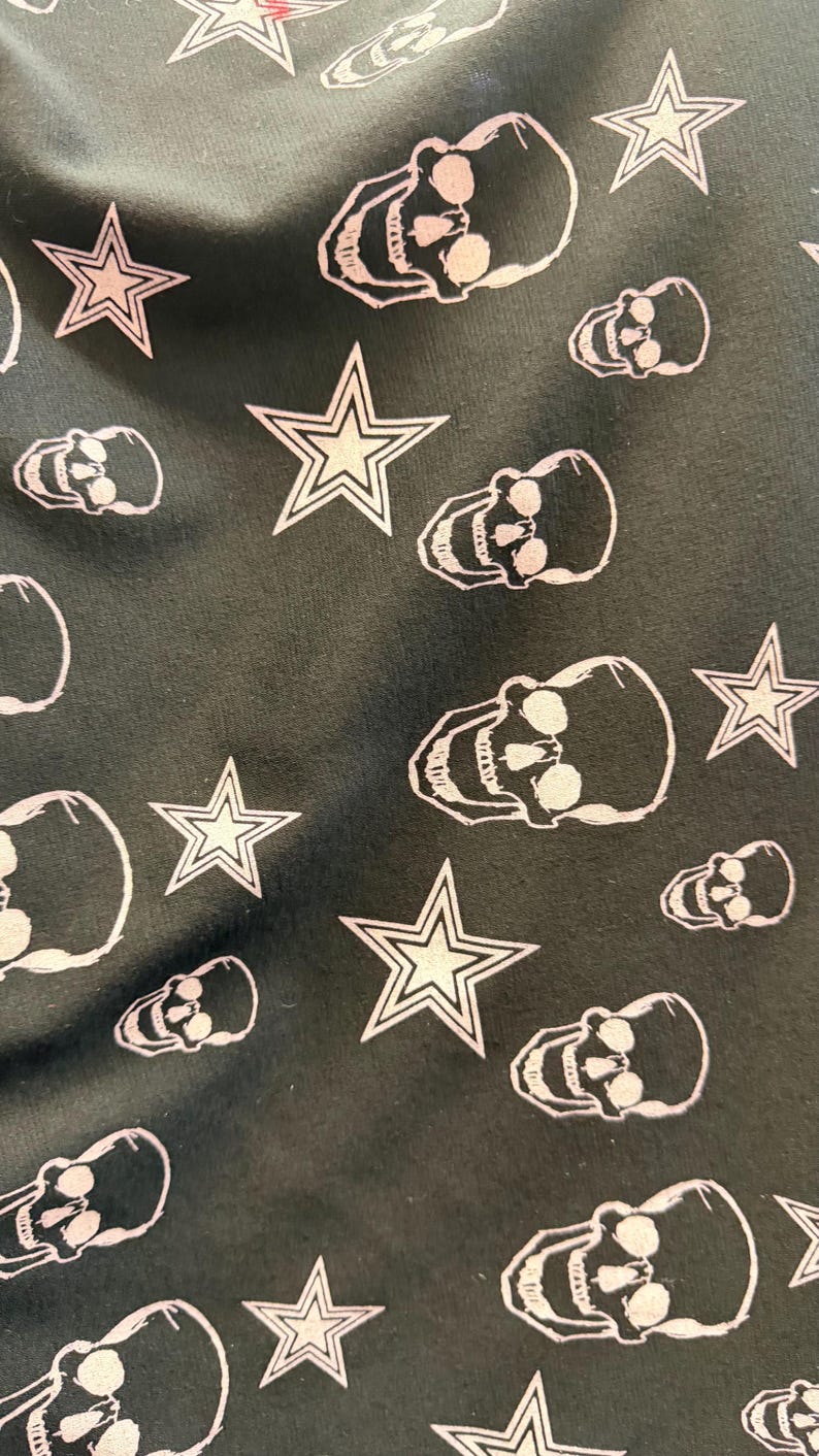 May include: Dark fabric featuring a repeating pattern of white skulls and stars. The skulls have open eye sockets and teeth. The stars have a five-point design.
