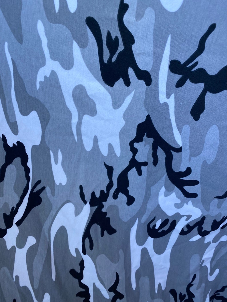 May include: A close-up of a grey and black camouflage pattern fabric. The fabric has a soft, textured feel and is ideal for creating unique clothing or accessories.