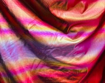 May include: Close-up of iridescent fabric with a holographic finish. The fabric is folded and draped, showing off the shimmering colors of pink, purple, gold, and red.
