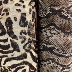 May include: Two rolls of fabric with animal print designs. One features a leopard print with brown spots on a beige background. The other has a snakeskin pattern in shades of brown and black.