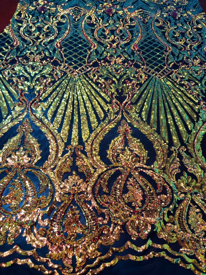 May include: A dark blue fabric with a gold and iridescent sequin pattern. The pattern features a repeating design of ornate swirls and leaves.