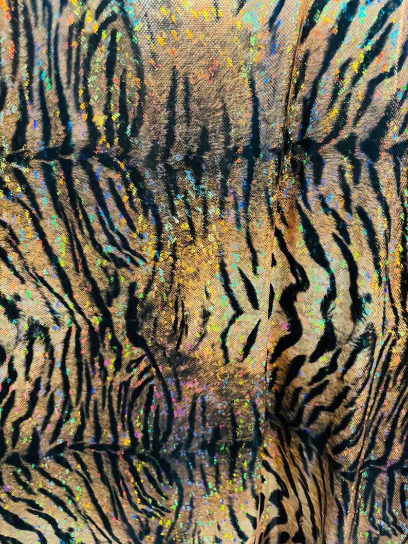 May include: A close-up of a brown and black tiger print fabric with iridescent glitter. The fabric has a shimmery, holographic effect.