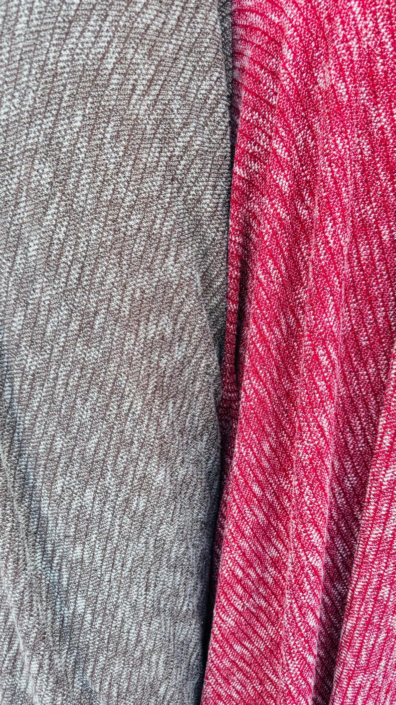K&ouml;nnte beinhalten: Nahaufnahme von zwei Stoffproben, eine grau und eine rot, mit einem wei&szlig;en, gefleckten Muster. Der Stoff hat eine strukturierte, gestrickte Optik.