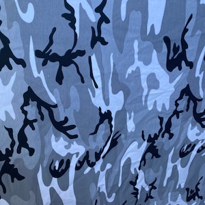 May include: A close-up of a grey and white camouflage fabric with black abstract shapes. The fabric has a soft, textured feel.