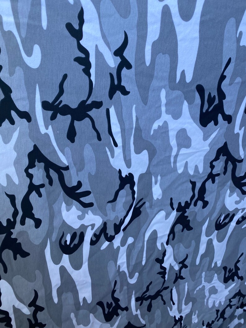 May include: A close-up of a grey and white camouflage fabric with black abstract shapes. The fabric has a soft, textured feel.