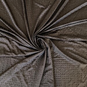Op de afbeelding: Een donkerbruine stof met een herhalend patroon van kleine, verhoogde, cirkelvormige stippen over het gehele oppervlak. Het materiaal is in het midden samengebracht, waardoor diepe plooien en draperingen ontstaan die de textuur en de consistente afstand tussen de stippen benadrukken.