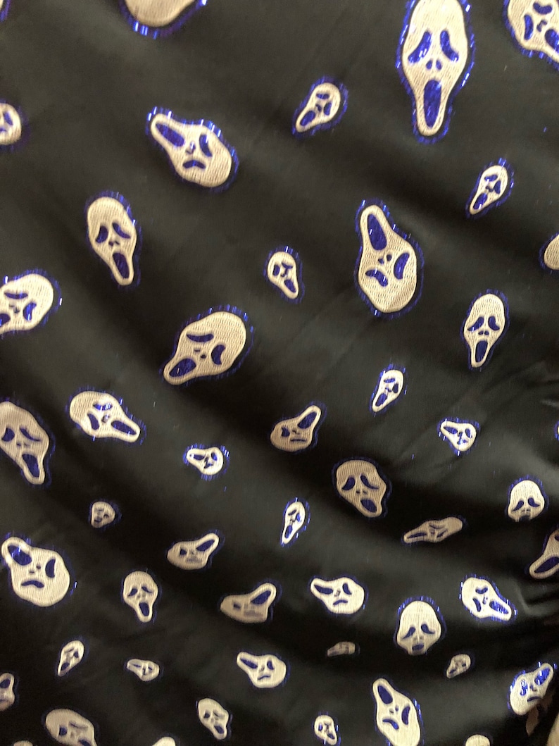 May include: Black fabric with a repeating pattern of white ghost faces with blue outlines. The ghost faces are all screaming.