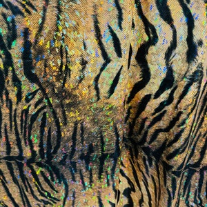 May include: Close-up of a fabric with a tiger stripe pattern. The fabric is iridescent and has a glittery finish.