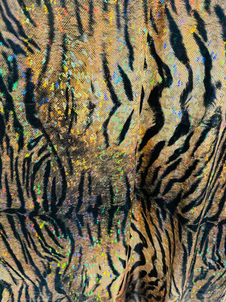 May include: Close-up of a fabric with a tiger stripe pattern. The fabric is iridescent and has a glittery finish.