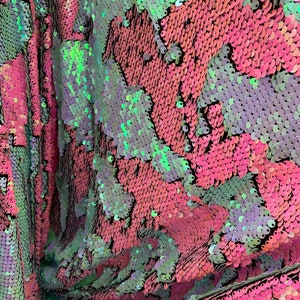 May include: Close-up of iridescent pink and green sequins on fabric. The sequins are arranged in a pattern of overlapping scales.
