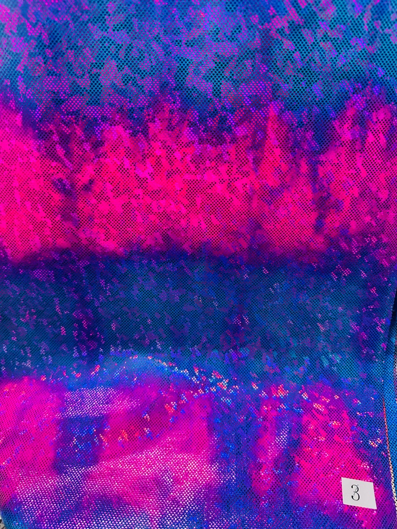 Op de afbeelding: Een close-up van een iriserende stof met een blauwe, roze en paarse kleurverloop. De stof heeft een textuur met een rasterpatroon.