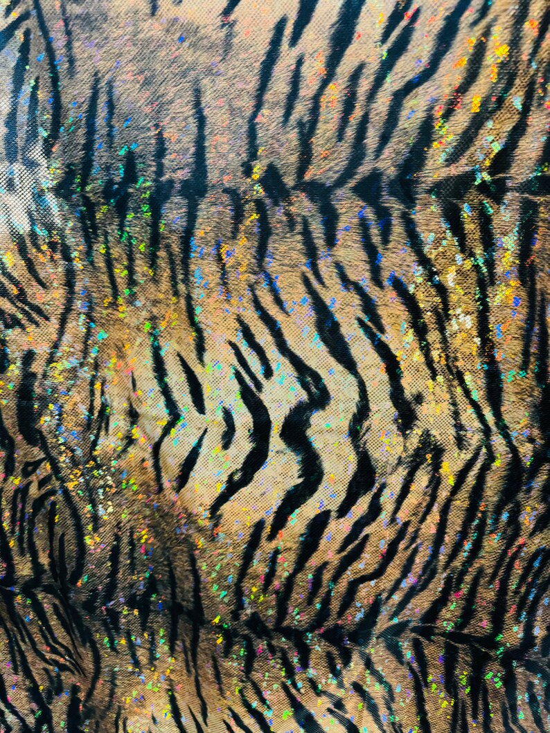 May include: Close-up of a fabric with a tiger stripe pattern. The fabric is brown and black with a glittery finish. The glitter is iridescent and has a rainbow effect.