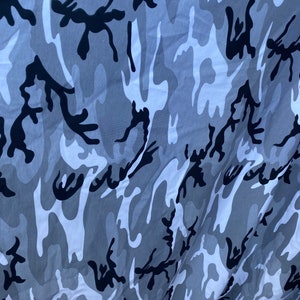 May include: A close-up of a grey and black camouflage fabric. The fabric has a wavy pattern with black and grey shapes.