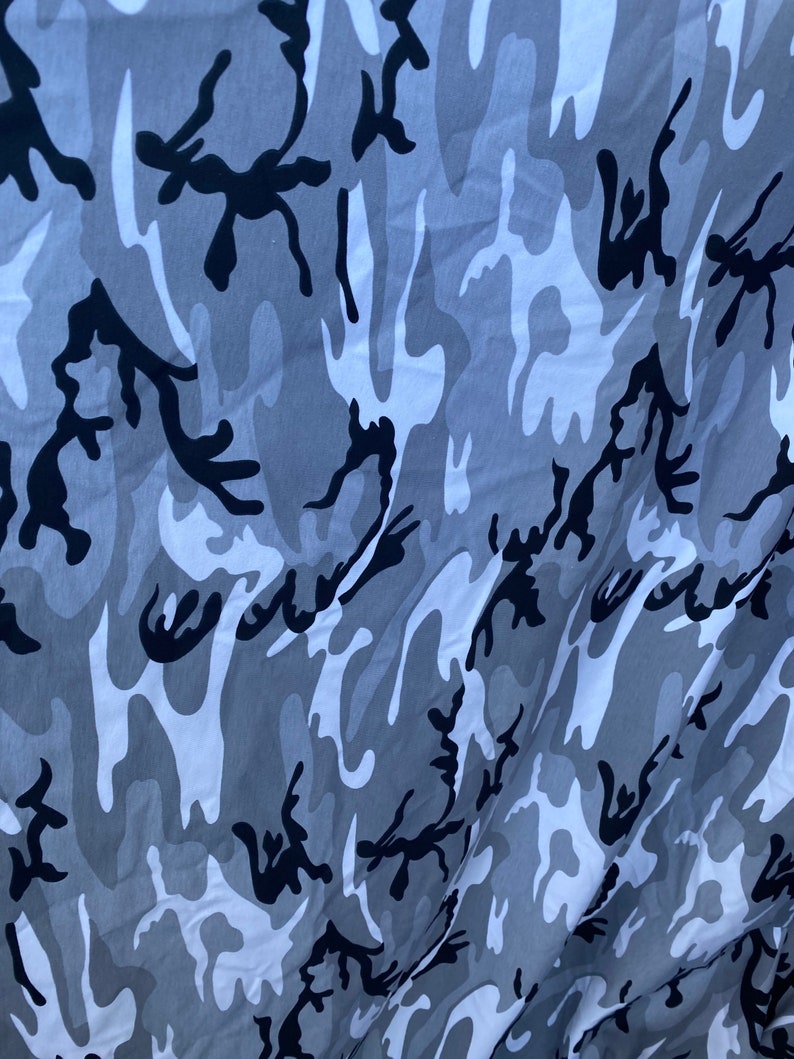 May include: A close-up of a grey and black camouflage fabric. The fabric has a wavy pattern with black and grey shapes.