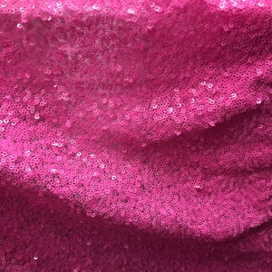 May include: Pink sequined fabric with a subtle shimmer. The sequins are closely packed together, creating a smooth and luxurious texture.
