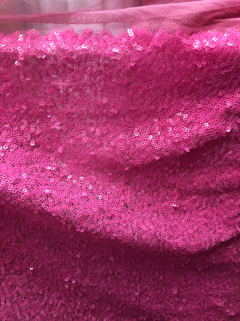 May include: Pink sequined fabric with a subtle shimmer. The sequins are closely packed together, creating a smooth and luxurious texture.