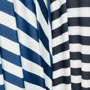 K&ouml;nnte beinhalten: Nahaufnahme von drei Stoffen mit kr&auml;ftigen, horizontalen Streifen. Ein Stoff weist marineblaue und wei&szlig;e Streifen auf, w&auml;hrend ein anderer schwarz-wei&szlig;e Streifen zeigt. Die Stoffe sind drapiert und erzeugen weiche Falten und Schatten.