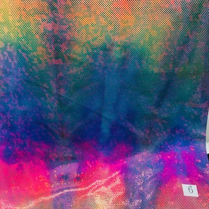 Op de afbeelding: Een close-up van een iriserende stof met een regenboogpatroon en een klein wit label met het nummer "6" erop.