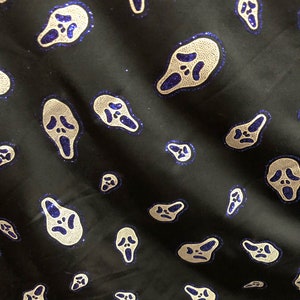 May include: Black fabric with a repeating pattern of white and blue glitter ghost faces. The ghost faces are in a scream pose with their mouths open.