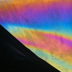 May include: A close-up of iridescent holographic fabric with a textured surface. The fabric is folded in a triangular shape, revealing a black background.