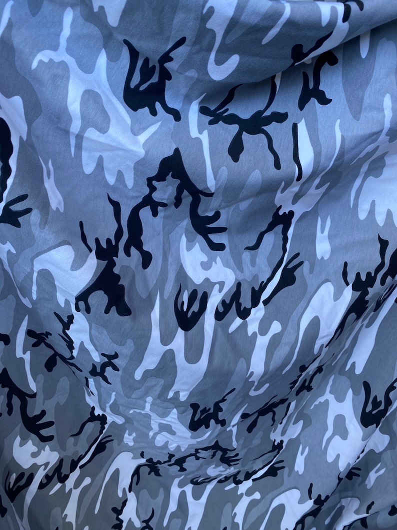 May include: Grey and black camouflage fabric with a wavy pattern. The fabric is folded and has a soft, textured feel.