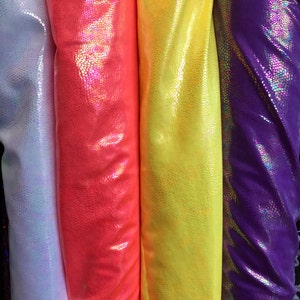 Puede incluir: Primer plano de varios rollos de tela en colores vibrantes. Las telas incluyen blanco, rojo brillante, amarillo y morado, cada una con un patrón texturizado en forma de escamas. El material tiene un acabado brillante e iridiscente, que refleja la luz.