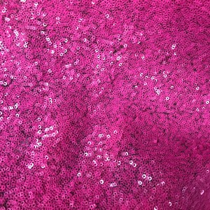 May include: A close-up of a fabric covered in pink sequins. The sequins are small and tightly packed together, creating a shimmering effect.