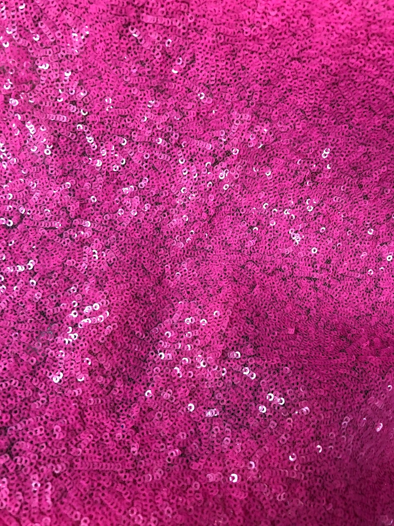 May include: A close-up of a fabric covered in pink sequins. The sequins are small and tightly packed together, creating a shimmering effect.