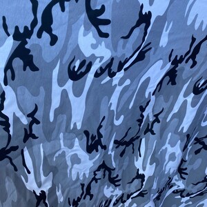 May include: A close-up of a grey, white and black camouflage fabric. The fabric has a swirling pattern.