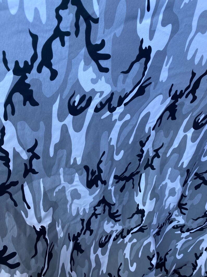 May include: A close-up of a grey, white and black camouflage fabric. The fabric has a swirling pattern.