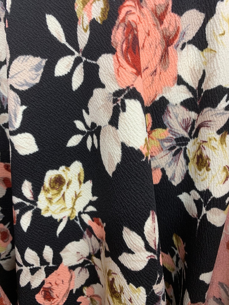 May include: Black fabric with a floral pattern featuring pink, white, and brown roses. The fabric has a textured surface.