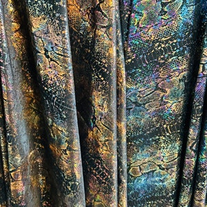 May include: Close-up of iridescent fabric with a snakeskin pattern in shades of gold, blue, and purple. The fabric is folded and has a textured, shiny surface.