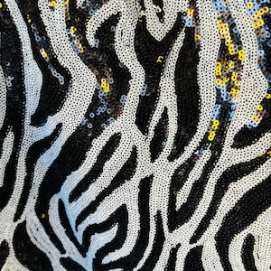 Könnte beinhalten: Schwarz-weißes Zebra-Musterstoff mit Pailletten. Die Pailletten sind in verschiedenen Farben, darunter Blau, Gold und Silber.