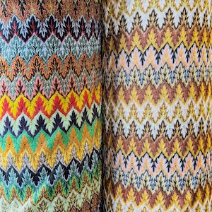 May include: Two rolls of fabric featuring a colourful chevron pattern. The fabric is woven with a variety of colours, including green, yellow, orange, red, brown, and white. The fabric is ideal for crafting, sewing, and home decor projects.