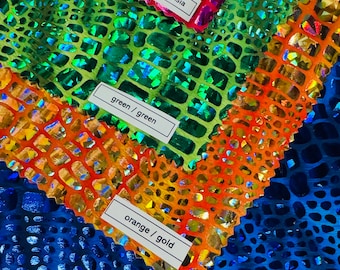 Op de afbeelding: Vier stofstalen met een schitterend krokodilleerpatroon. De stalen zijn gelabeld met "helder roze / fuchsia", "groen / groen", "oranje / goud" en "blauw / blauw".