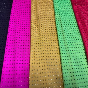Op de afbeelding: Zes verticale stroken stof in zwart, felroze, goud, limoengroen, rood en donkerblauwgroen. Elke strook is voorzien van een uniform raster van kleine, reflecterende, ronde studs of strass-steentjes die een consistent, herhalend patroon vormen.