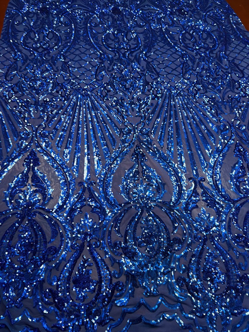 Puede incluir: Tela azul real con lentejuelas con un patr&oacute;n de damasco. Las lentejuelas est&aacute;n dispuestas en un patr&oacute;n repetitivo de remolinos y hojas.