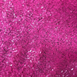 May include: Close-up of a fabric with a pink sequin pattern.