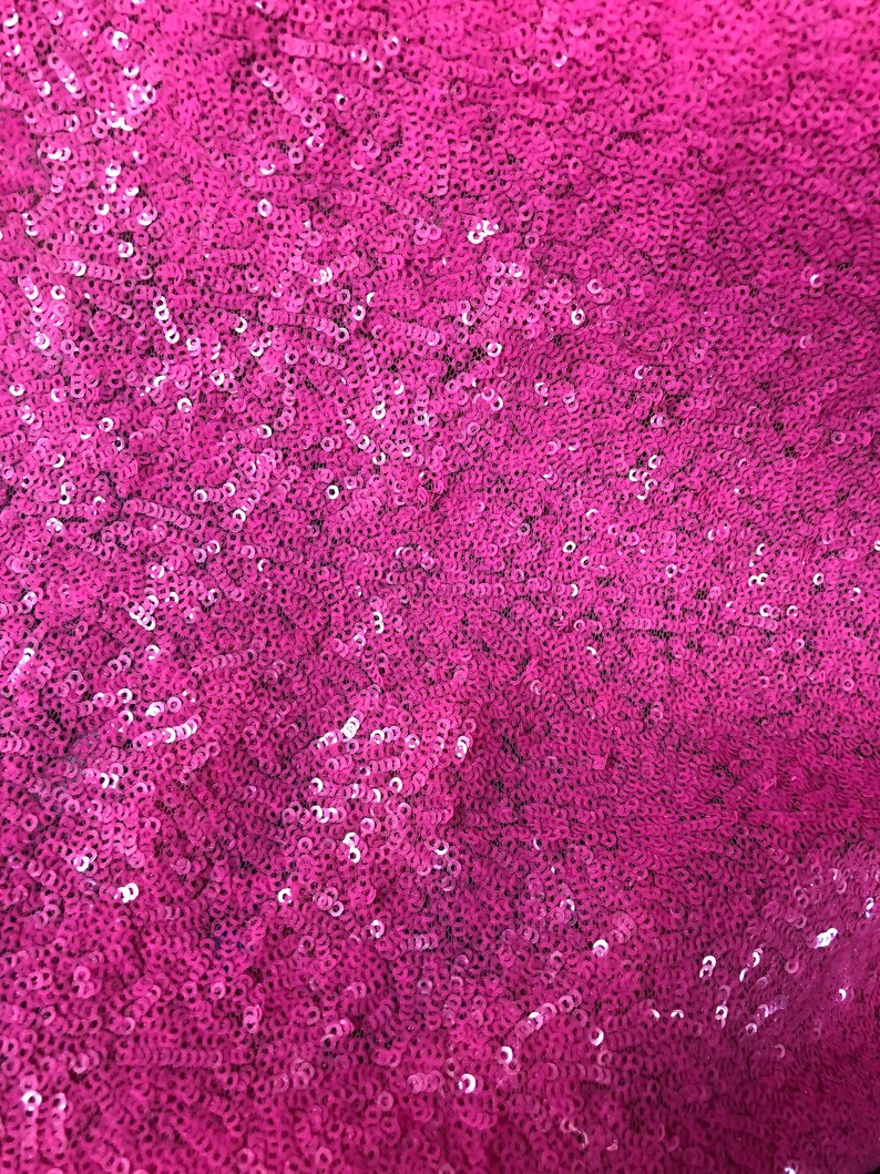 May include: Close-up of a fabric with a pink sequin pattern.