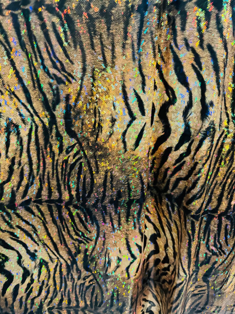 May include: A close-up of a fabric with a tiger stripe pattern. The fabric is brown and black with iridescent glitter accents.