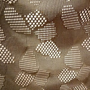 Könnte beinhalten: Ein dunkelgrauer Stoff mit einem sich wiederholenden geometrischen Muster aus unregelmäßigen, abgerundeten Formen. Jede Form ist mit einem Gitter aus kleinen kreisförmigen Ausschnitten gefüllt, was eine perforierte Textur erzeugt.