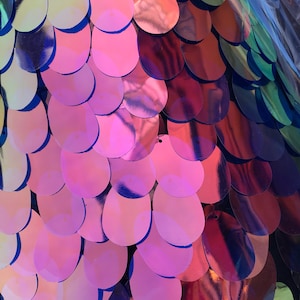 Könnte beinhalten: Nahaufnahme von schimmernden rosa, violetten und blauen Pailletten, die in einem Fischschuppenmuster auf einem schwarzen Stoffhintergrund angeordnet sind.