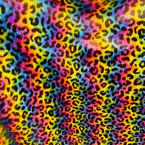 Puede incluir: Una tela colorida con un estampado de leopardo. La tela es un arcoíris de colores, incluyendo amarillo, naranja, rojo, rosa, azul, verde y morado. Las manchas de leopardo son negras y están dispersas por la tela.
