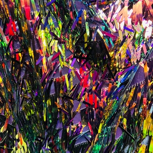 May include: Close-up of a fabric with iridescent sequins in shades of green, yellow, red, and purple. The sequins are arranged in a layered, textured pattern, creating a shimmering effect. The background is a dark purple fabric.
