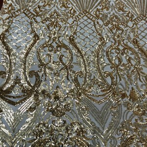 May include: Gold sequin fabric with a white mesh backing. The fabric features a damask pattern with a repeating design of swirls and leaves.