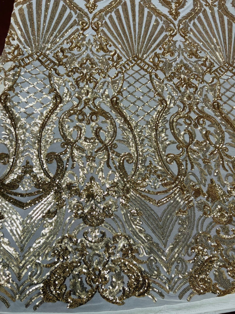 May include: Gold sequin fabric with a white mesh backing. The fabric features a damask pattern with a repeating design of swirls and leaves.