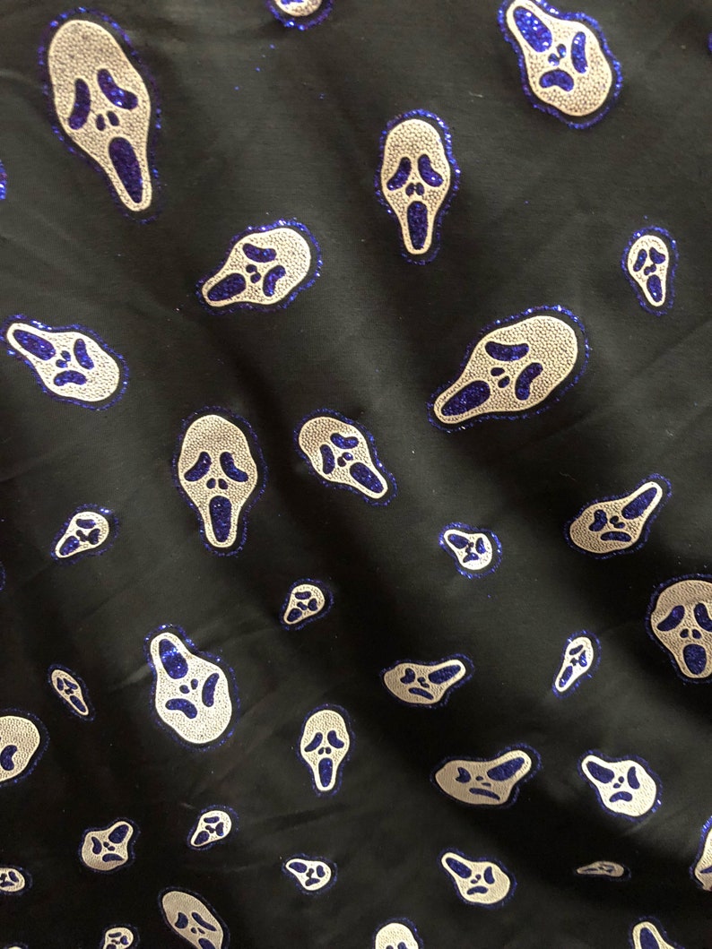 May include: Black fabric with a repeating pattern of white ghost face masks with blue glitter accents.