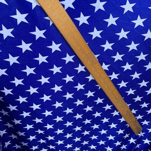 May include: Blue fabric with a white star pattern. A wooden ruler with markings in inches is placed diagonally across the fabric.