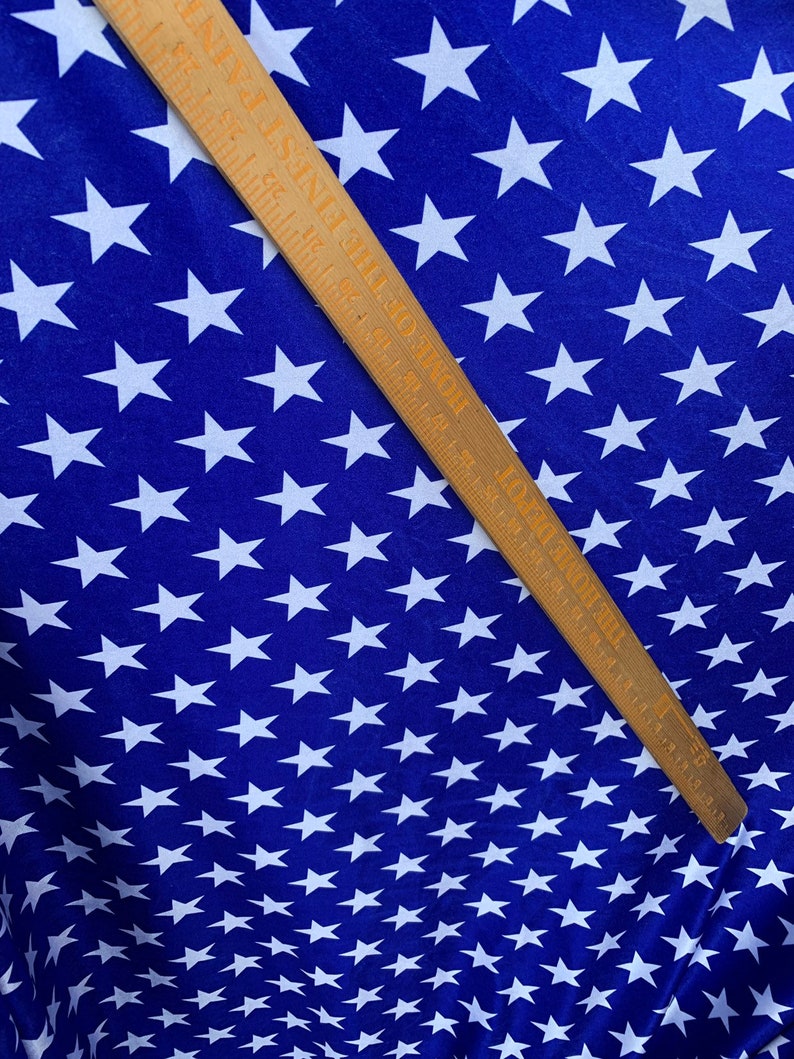 May include: Blue fabric with a white star pattern. A wooden ruler with markings in inches is placed diagonally across the fabric.